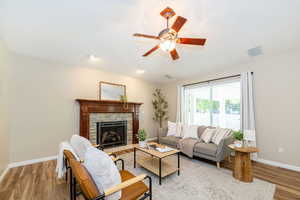 Living room with light wood-type flooring, baseboards, ceiling fan, and a fireplace
