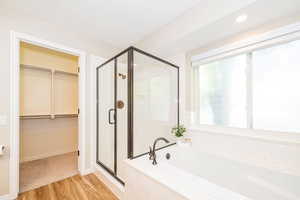 Bathroom featuring a stall shower, a bath, a spacious closet, and wood finished floors