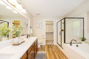 Full bathroom with a shower stall, double vanity, a bath, and wood finished floors