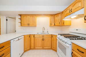 Kitchen with white appliances, under cabinet range hood, a sink, and light countertops