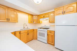 Kitchen with white appliances, a sink, under cabinet range hood, light countertops, and light flooring