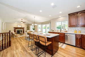 Kitchen with stainless steel dishwasher, a kitchen bar, light wood-type flooring, a fireplace, and recessed lighting