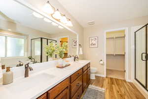 Full bath with a shower stall, double vanity, a walk in closet, wood finished floors, and toilet