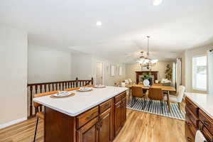 Kitchen with light wood-style flooring, light countertops, a chandelier, a kitchen island, and baseboards