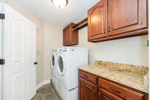 Laundry area with washing machine and clothes dryer, cabinet space, baseboards, and dark stone finish flooring