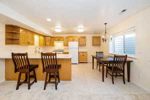 Kitchen featuring white appliances, a peninsula, light countertops, open shelves, and brown cabinets