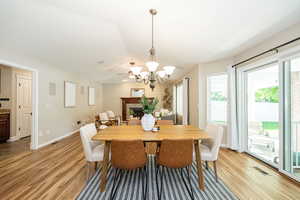 Dining space featuring light wood-style flooring, a chandelier, a stone fireplace, and baseboards