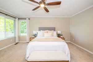 Bedroom with light colored carpet, ornamental molding, baseboards, and ceiling fan