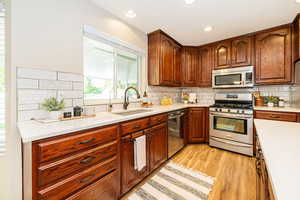 Kitchen featuring stainless steel appliances, a sink, backsplash, light wood-style floors, and light countertops