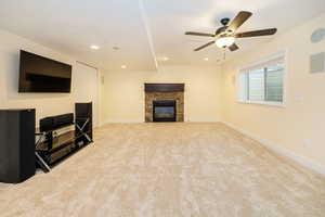 Unfurnished living room with light colored carpet, a ceiling fan, a stone fireplace, baseboards, and recessed lighting
