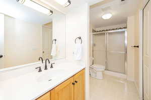 Full bathroom with toilet, a stall shower, vanity, and tile patterned floors