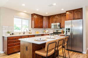 Kitchen featuring stainless steel appliances, a sink, light wood finished floors, a kitchen breakfast bar, and light countertops
