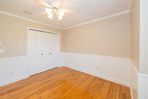 Unfurnished bedroom with light wood-type flooring, wainscoting, a closet, ornamental molding, and ceiling fan