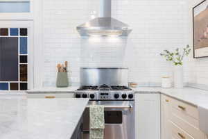 Kitchen featuring wall chimney exhaust hood, stainless steel gas range, and tasteful backsplash