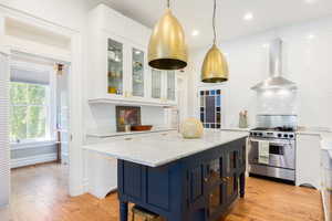 Kitchen featuring wall chimney range hood, stainless steel range with gas cooktop, white cabinets, decorative backsplash, and light wood-type flooring