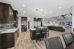 Kitchen with built in appliances, open floor plan, dark brown cabinets, a kitchen breakfast bar, and recessed lighting