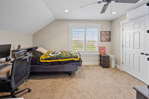 Bedroom featuring an AC wall unit, carpet flooring, vaulted ceiling, ceiling fan, and baseboards