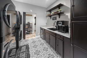 laundry room featuring a sink, stacked washer / dryer, dark brown cabinets, open shelves, and beverage cooler