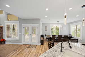 Dining room with french doors, light wood-type flooring, recessed lighting, baseboards, and a chandelier