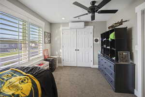 Bedroom with a wall mounted AC, a closet, carpet floors, ceiling fan, and baseboards