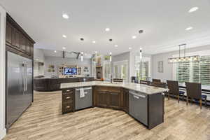 Kitchen with stainless steel appliances, two dishwashers, open floor plan, dark brown cabinets, light wood-style floors, and recessed lighting