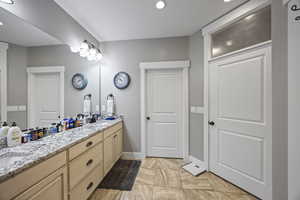 Bathroom featuring double vanity, baseboards, recessed lighting, and marble look tiles