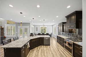 Kitchen featuring appliances with stainless steel finishes, a sink, light wood finished floors, tasteful backsplash, and dark brown cabinets