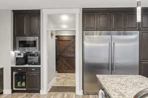 Kitchen featuring built in oversize appliances, dark brown cabinets, and light stone counters