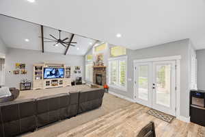 Living area featuring wood finished floors, ceiling fan, baseboards, a stone fireplace, and vaulted ceiling