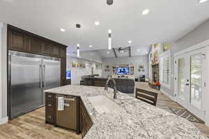 Kitchen with appliances with stainless steel finishes, a sink, dark brown cabinetry, a ceiling fan, and light wood-type flooring
