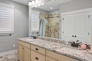 Full bath with double vanity, baseboards, and a tile shower