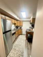 Kitchen featuring appliances with stainless steel finishes, a sink, light wood-style flooring, wall chimney range hood, and baseboards