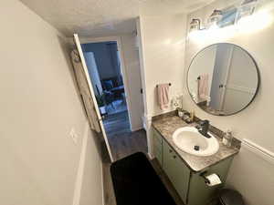 Bathroom with a textured ceiling, wood finished floors, vanity, toilet, and baseboards