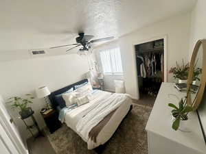 Carpeted bedroom featuring a spacious closet, a closet, a ceiling fan, a textured ceiling, and baseboards