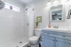 Full bath featuring toilet, vanity, tiled shower, and ceiling fan