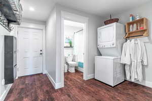 Washroom with stacked washing machine and dryer, wood finished floors, baseboards, and recessed lighting
