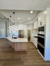 Kitchen featuring a large island, stainless steel appliances, white cabinetry, quartz countertops and decorative light fixtures