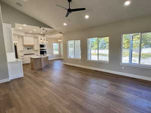 Great room featuring high vaulted ceiling, a fireplace, a ceiling fan, recessed lighting and tons of natural light - View into the kitchen