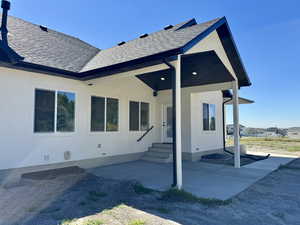 Back of property with a patio, roof with shingles, entry steps, and stucco siding