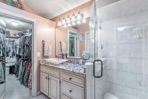 Bathroom featuring vanity, a walk in closet, a shower stall, lofted ceiling, and a textured ceiling