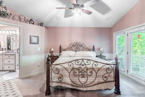 Bedroom with vaulted ceiling, access to outside, wainscoting, light carpet, and ensuite bathroom