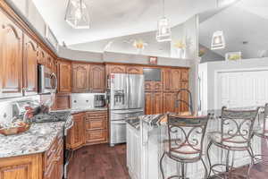 Kitchen featuring appliances with stainless steel finishes, high vaulted ceiling, brown cabinetry, dark wood-style floors, and light stone countertops