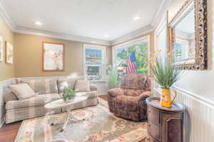 Living area with wood finished floors, crown molding, wainscoting, recessed lighting, and a textured ceiling