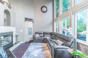 Living room featuring a high ceiling, baseboards, a tiled fireplace, and dark wood-style flooring