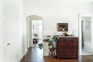 Hallway with arched walkways, dark wood-style flooring, and baseboards