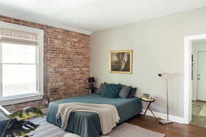 Bedroom featuring wood finished floors, brick wall, and baseboards