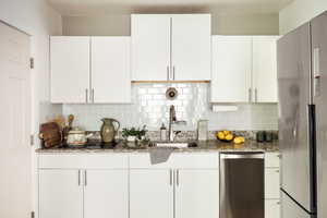 Kitchen with stainless steel appliances, a sink, white cabinets, and light stone countertops