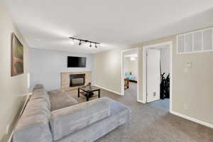 Carpeted living area featuring rail lighting, a stone fireplace, and baseboards