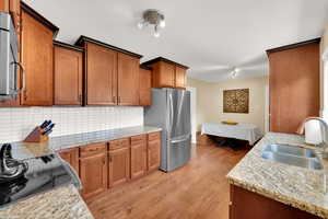 Kitchen with appliances with stainless steel finishes, a sink, backsplash, light wood finished floors, and brown cabinets