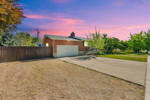 View of front of property featuring a garage, concrete driveway, a chimney, and brick siding